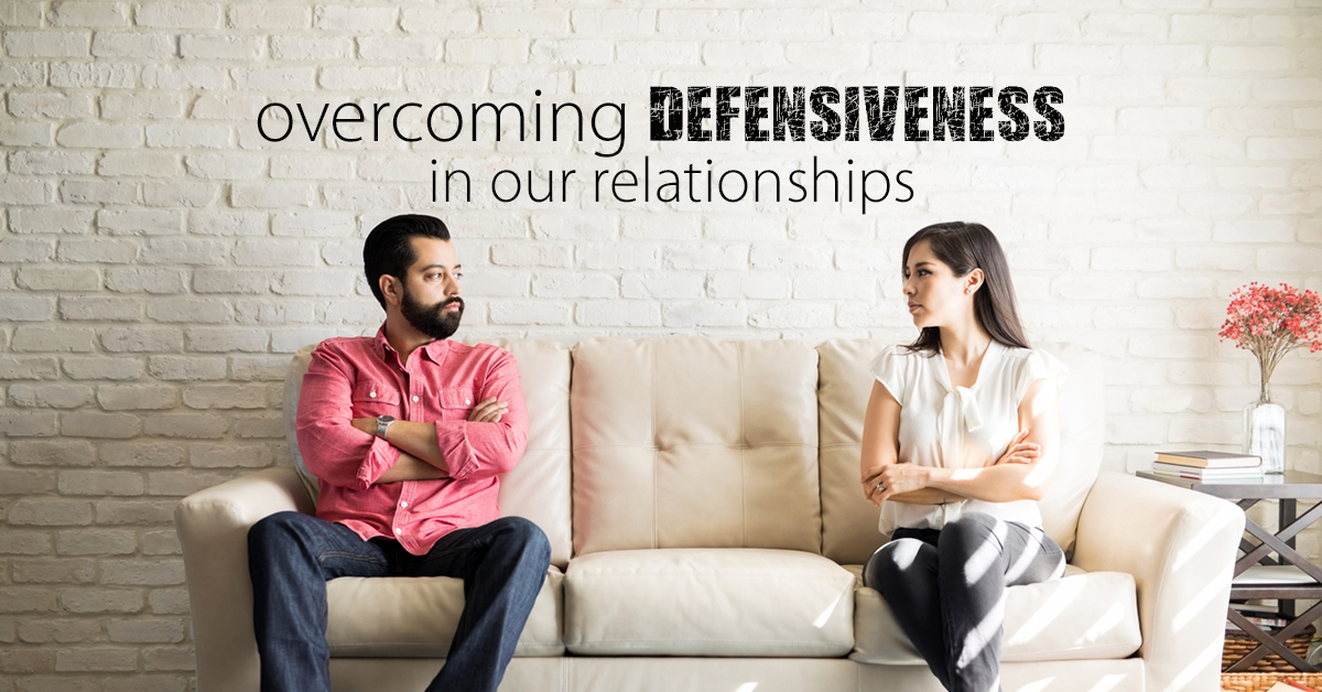 defensive couple on couch with arms crossed and the words "overcoming defensiveness in our relationships" in words above it