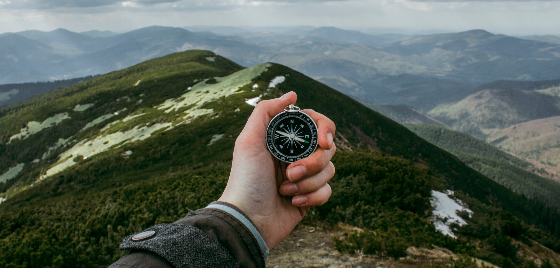 hand holding a compass in front of a mountain